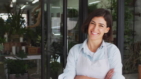 retrato de una mujer sonriente dueña de floristas de pie en la puerta rodeada de plantas