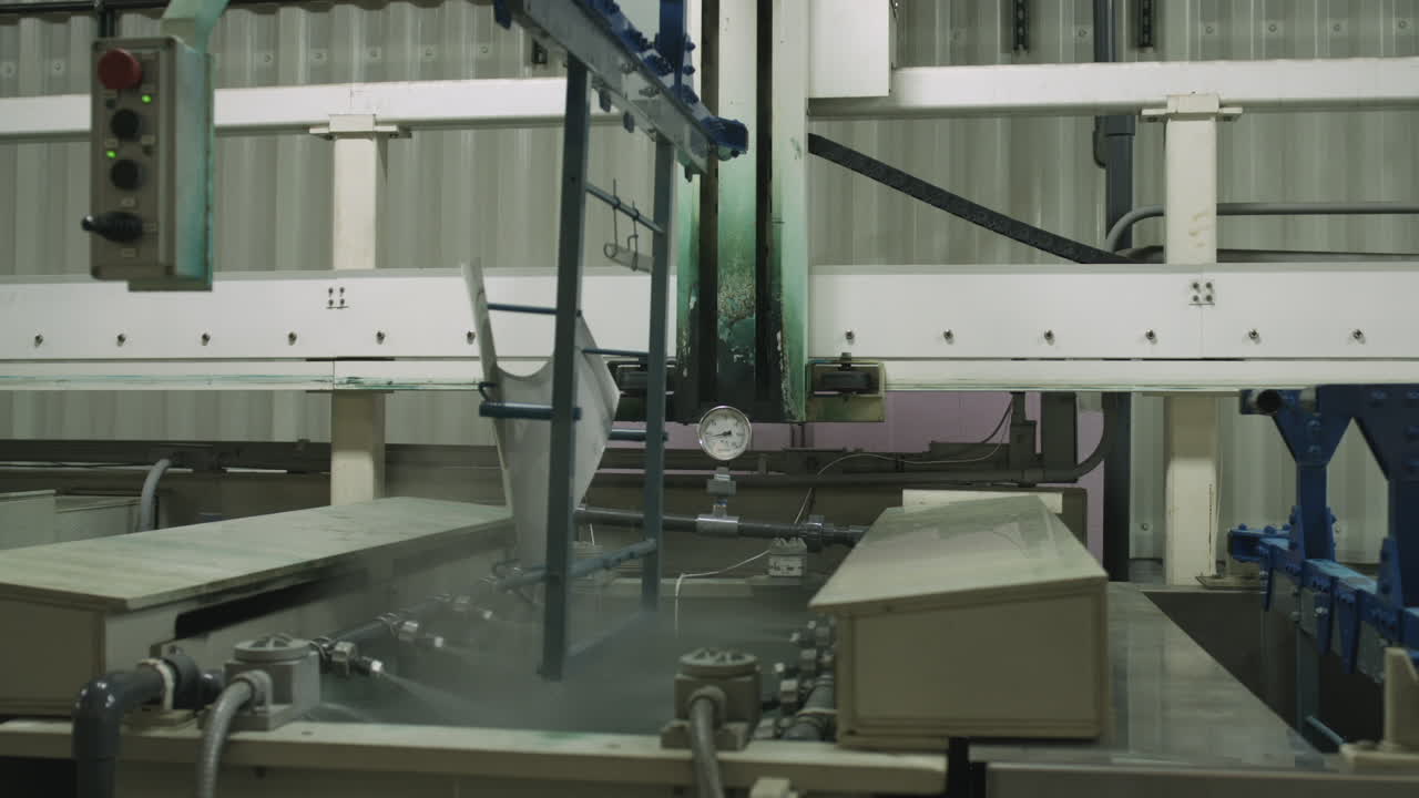 Slider shot of machine lifting metal part from chemical bath and spraying off excess coating