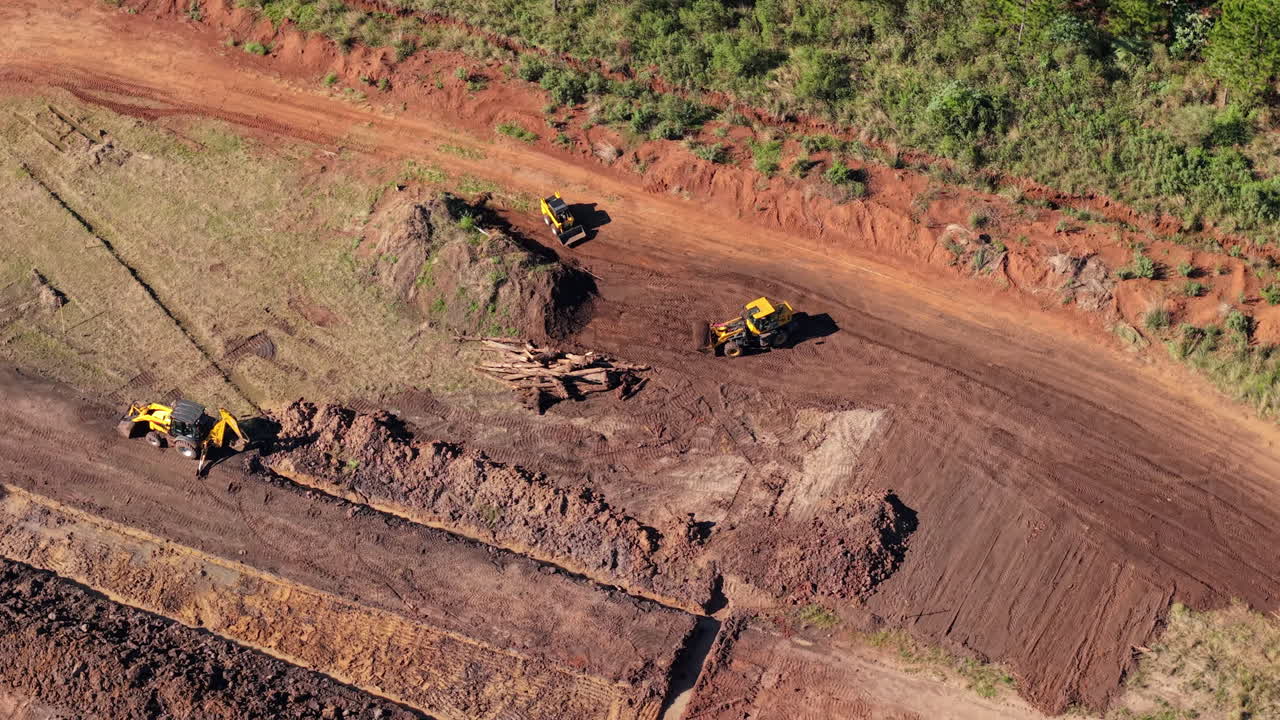 Aerial clip captures heavy machinery reshaping terrain amid vegetation under bright sunlight. Ideal for construction progress reels or equipment showcases.
