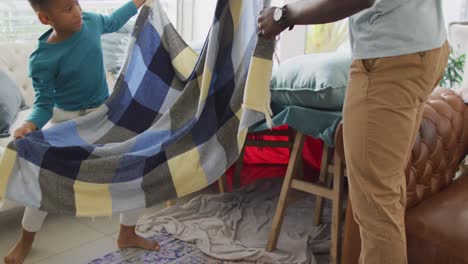 Video-Des-Mittelteils-Eines-Afroamerikanischen-Vaters-Und-Sohnes,-Der-Die-Basis-Aus-Stühlen-Und-Einer-Decke-Vorbereitet