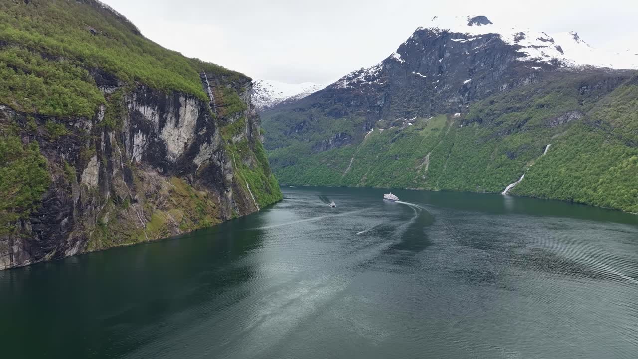 um navio de cruzeiro e um ferry turístico local estão se encontrando no fiorde de geiranger, na noruega, durante o mês de maio e primavera, com colinas verdes e montanhas cobertas de neve - imagem aérea acima do fiorde
