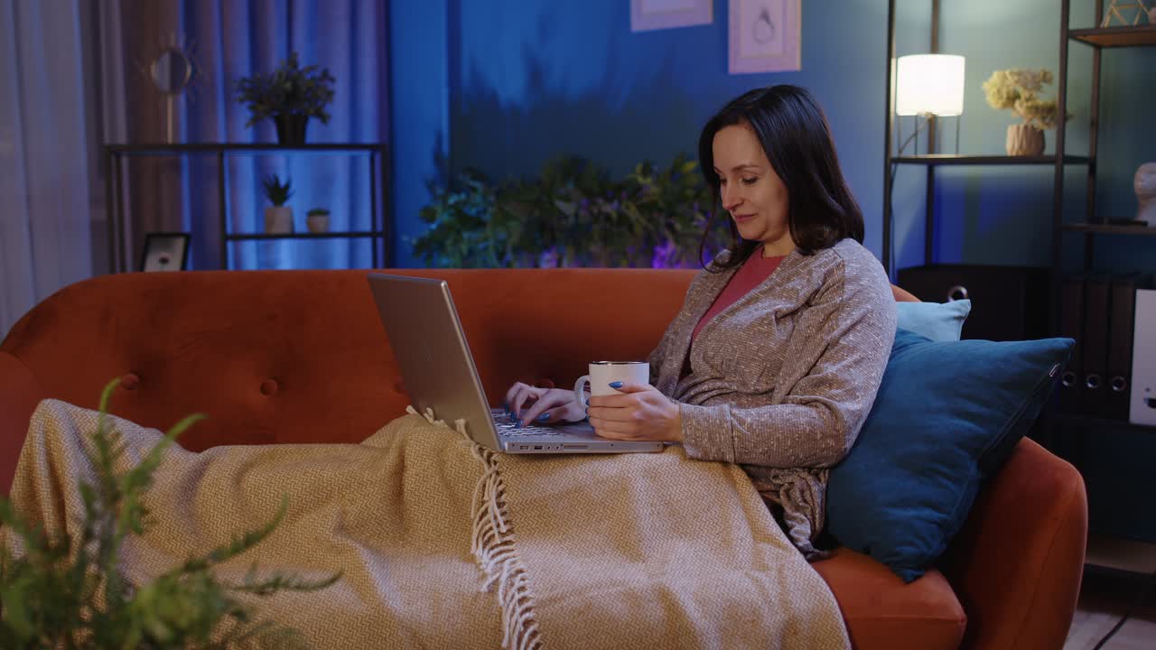 Woman freelancer lying on sofa working on laptop notebook shopping studying online at home alone