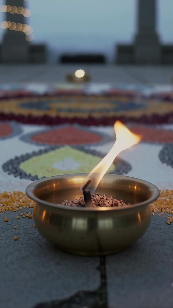 Vertical video: Moving shot focusing on brass bowl on terrace rangoli, flame flickering from breeze
