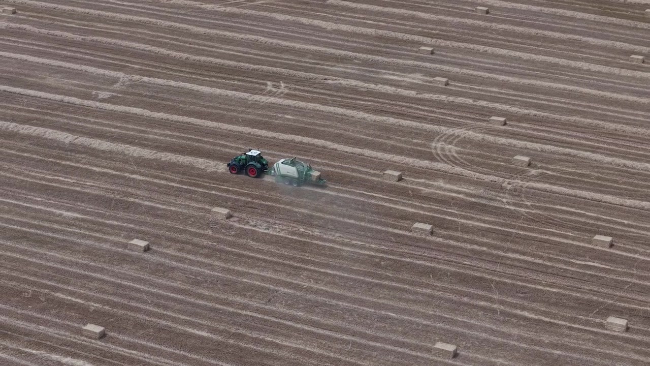 Una ripresa aerea di un trattore che traina una pressa per balle attraverso un grande campo raccolto durante la stagione agricola estiva