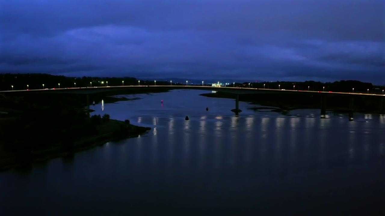 Stoupající letecký záběr řeky Foyle a mostu Foyle s nočním provozem; atmosférický úvodní záběr.
