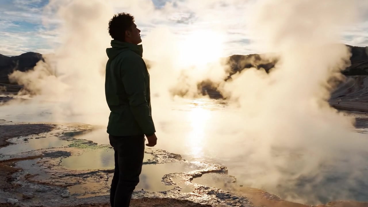 Una figura solitaria in piedi in un paesaggio geotermico fumante, che osserva l'alba radiosa riflessa nell'acqua, catturando la bellezza delle meraviglie della natura.