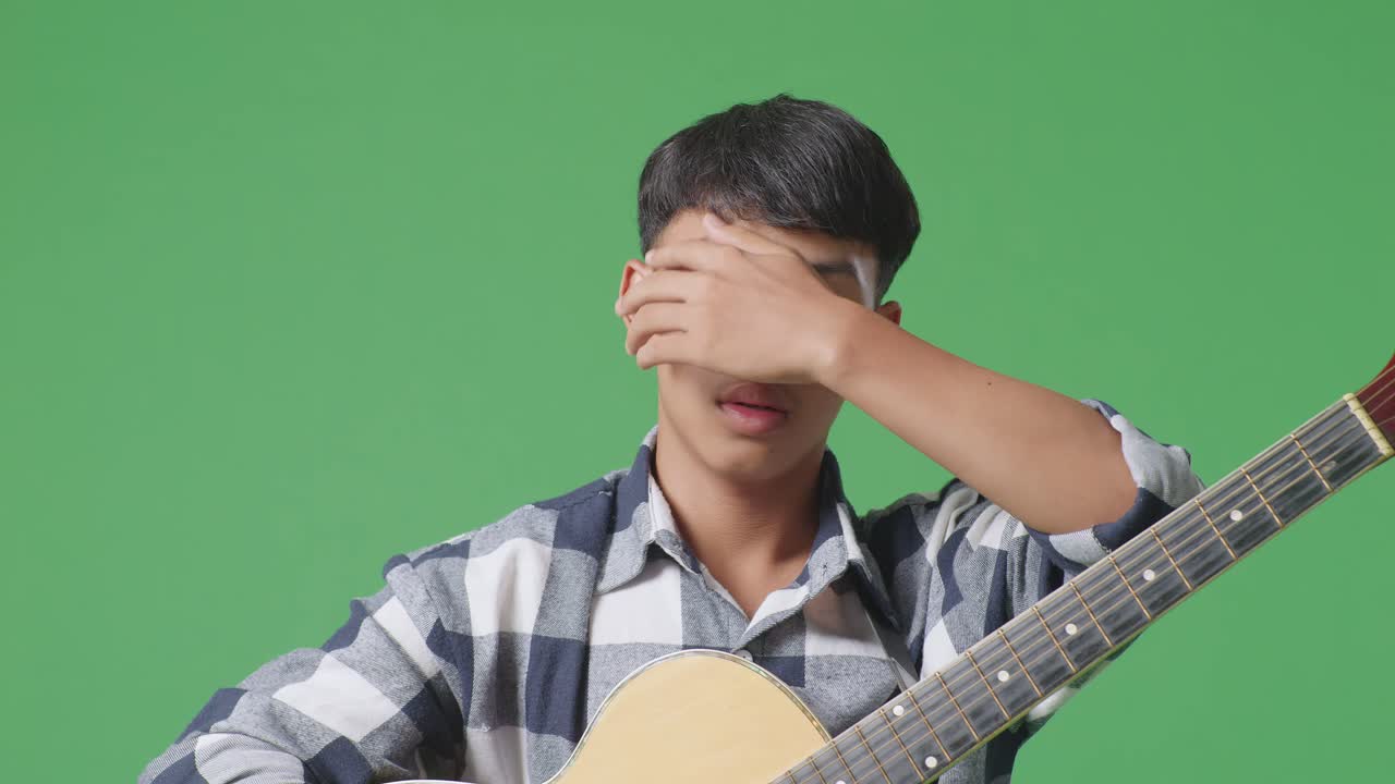 녹색 화면 배경 에 서 있는 기타 를 들고 있는 피곤 한 아시아 청소년 의 근접 사진