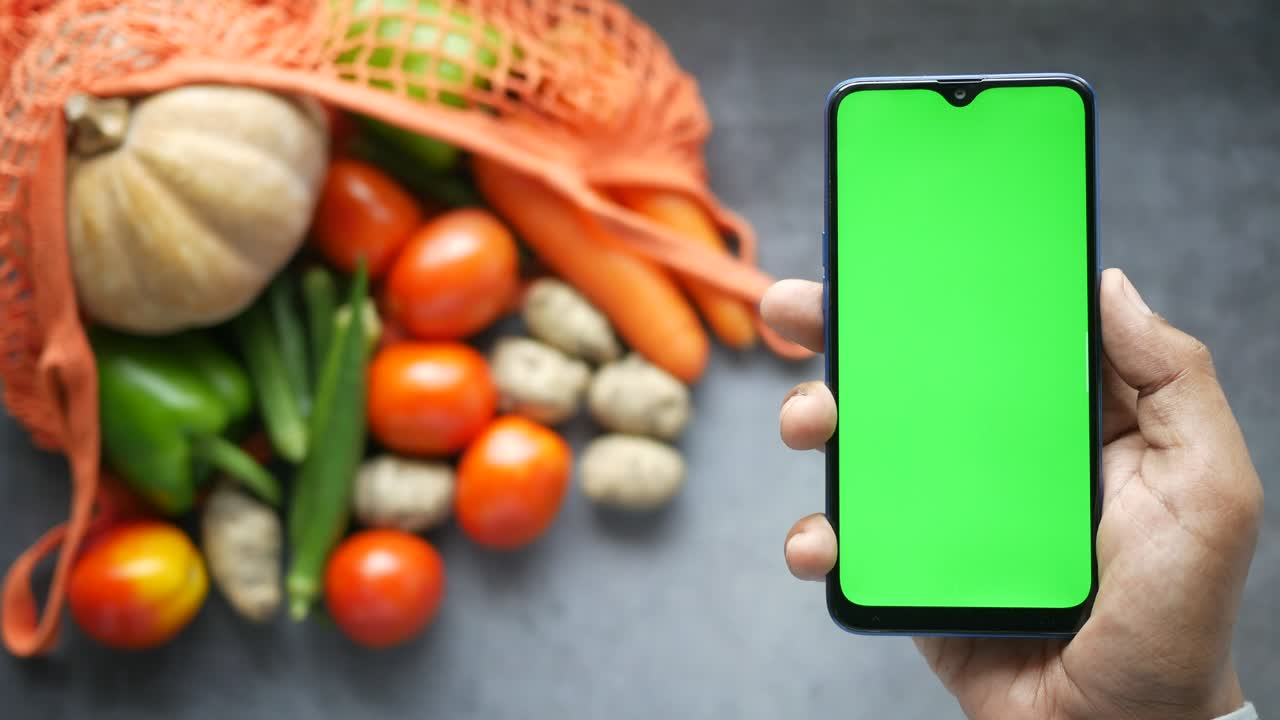 vista superior de la mano del hombre sosteniendo un teléfono inteligente con verduras frescas en la mesa
