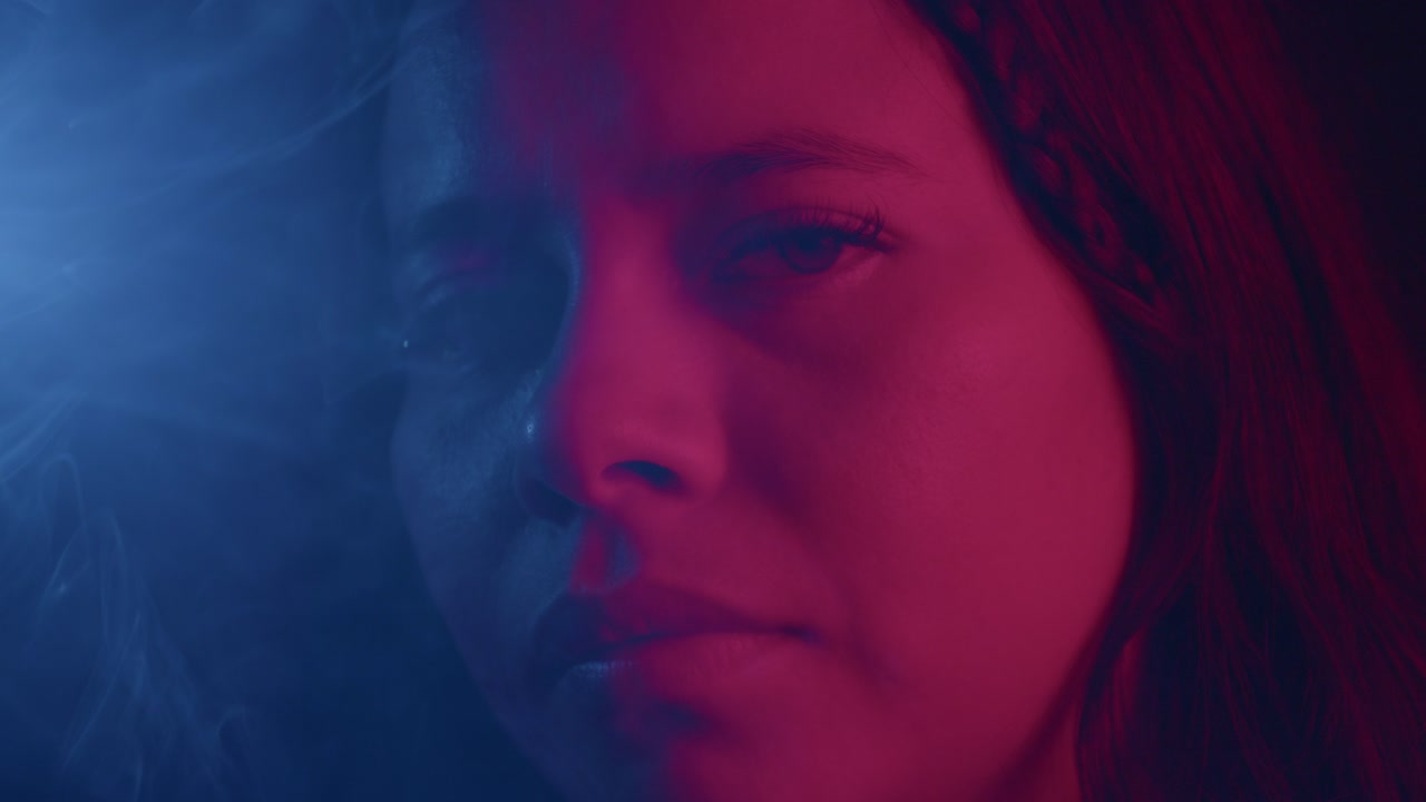 Close-up shot of a pensive face bathed in dramatic red and blue lighting, creating a mysterious mood. The contrasting colors and soft focus add intrigue to this cinematic scene
