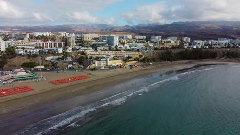 Vídeo-Cinematográfico-Aéreo-De-Drones-4k-De-La-Playa-Y-El-Mar-De-Maspalomas-En-Una-Mañana-Tranquila,-Con-Hermosas-Montañas-De-Gran-Canaria-Al-Fondo