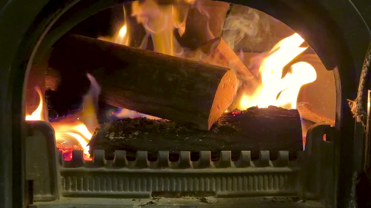 Fiamme arancioni brillanti avvolgono ceppi di legno all'interno di una stufa in ghisa nera con sportello in vetro