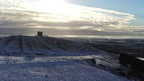 Snowy-Rivington-Pike-Tower-Winter-Hill-Vista-Aérea-Gente-Trineo-Cuesta-Abajo-Al-Amanecer-Subiendo-A-La-Izquierda