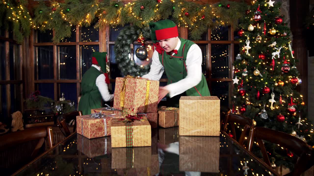 Happy elves working with Christmas presents. Elves put gift boxes on the table in the Christmas decorated room in Santa's residence