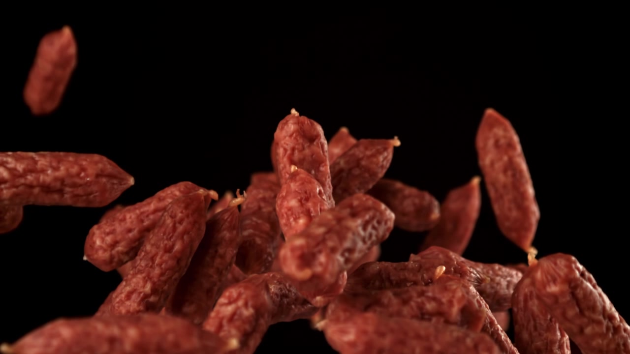 Mini salsicce di salame che cadono al rallentatore su sfondo nero.