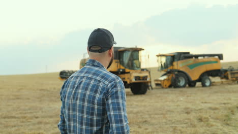 agricultor exitoso trabajando en una computadora portátil y mirando máquinas cosechadoras