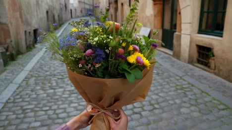 person holding a colorful flower bouquet on an old cobblestone street