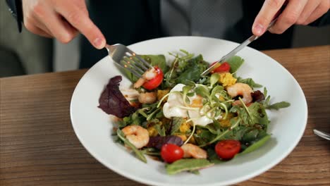 close-up of male hands cutting shrimp from salad with tomatoes and greens