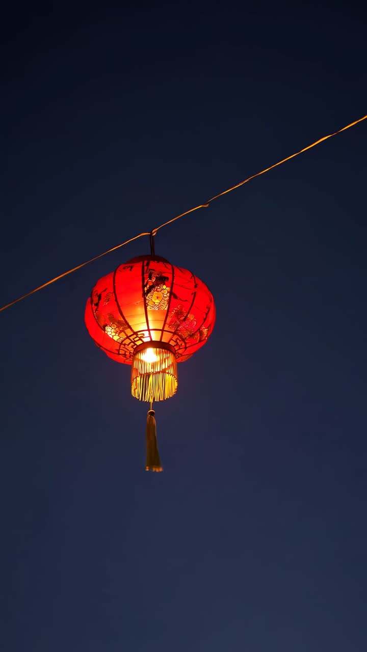 Low-angle shot of a glowing red lantern against a dark sky, capturing a serene, festive ambiance