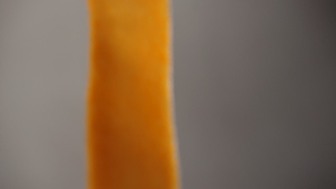 슬로우 모션 샷으로 카메라 앞에서 움직이는 주황색 고구마의 매우 얇은 스트립 클로즈업