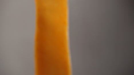 close-up of a very thin strip of orange sweet potato, moving in front of the camera in slow motion shot