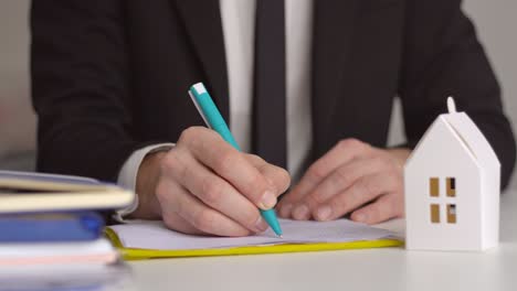 close up of real estate agent working sign agreement document contract for home loan insurance approving purchases for client with paper house model.