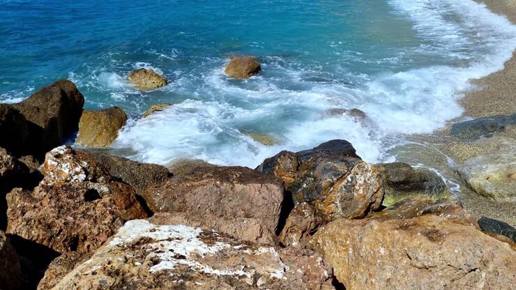 Inquadratura statica e serena di onde del mare che si infrangono sugli scogli e sulla spiaggia nella splendida località costiera di Varigotti, nel nord Italia.