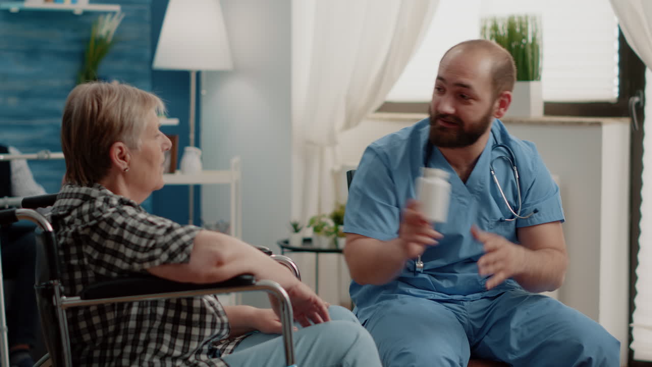 Old woman in wheelchair receiving bottle of pils from man nurse