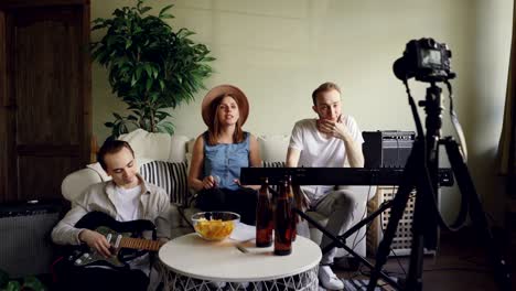 young members of popular band are recording video for online blog with camera. attractive female vocalist is talking holding microphone, her friends are smiling.