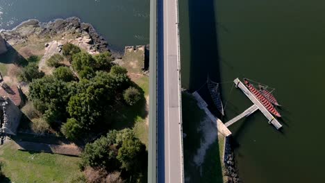 Autos,-Die-über-Die-Brücke-über-Den-Fluss-Ulla-Fahren,-Mit-Wikingerbooten-Auf-Dem-Steg-Darunter,-Sonniger-Nachmittag,-Drohnenaufnahmen,-Die-Den-Zenit-Vorwärts-Bewegen