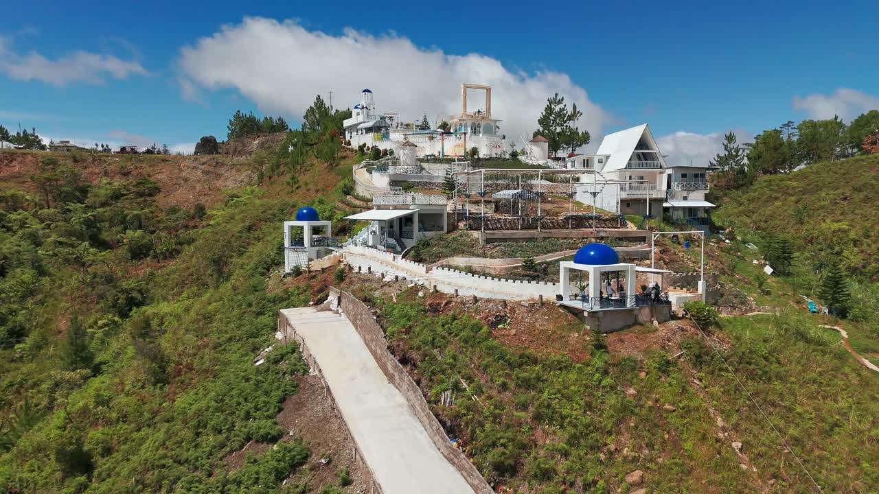 Cinematic 4K drone rising reveal of white hillside architecture with blue domes surrounded by lush greenery and blue sky in the Philippines, ideal for travel, tourism, and cultural projects