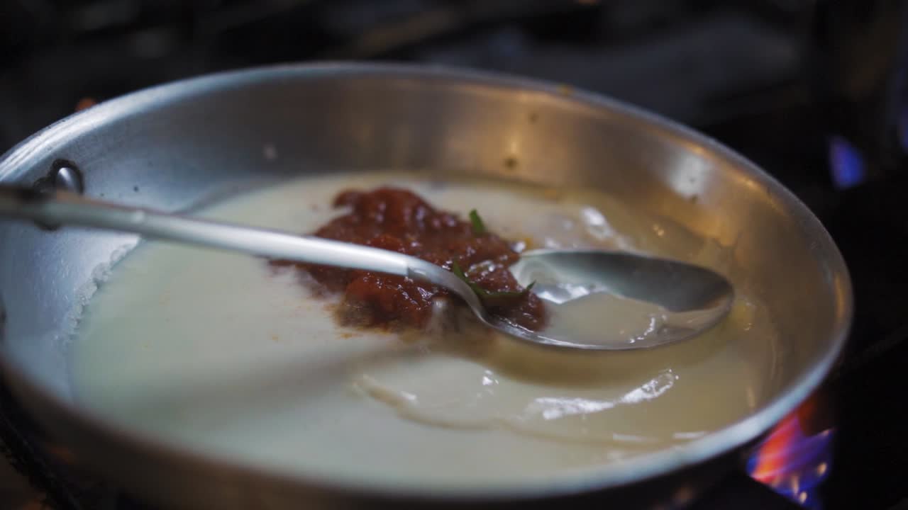 el chef enciende la estufa de gas y pone hierbas frescas en la salsa para el plato de pasta