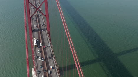 Vista-Frontal-Del-Control-Deslizante-Aéreo-Del-Tráfico-Denso-De-Vehículos-Múltiples-A-Través-Del-Famoso-Puente-De-Suspensión-Roja-Grande-Ponte-25-De-Abril-En-Lisboa,-Portugal