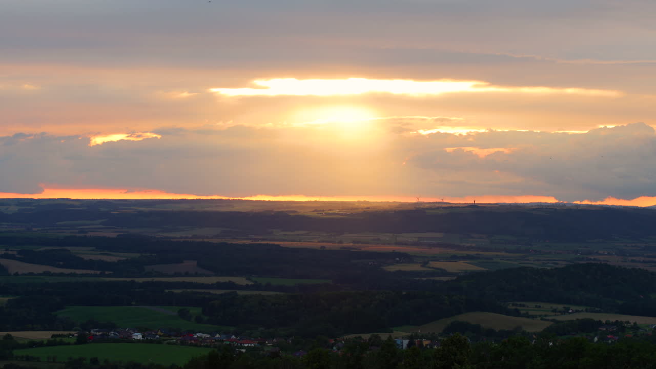 수평선 위로 움직이는 다양한 색상의 구름 아래 누워 있는 풍경에 광선이 반사되어 일몰 동안 구름 사이로 빛나는 태양