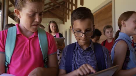 Niño-Y-Niña-Discutiendo-Sobre-Una-Tableta-Digital-En-El-Pasillo-De-La-Escuela