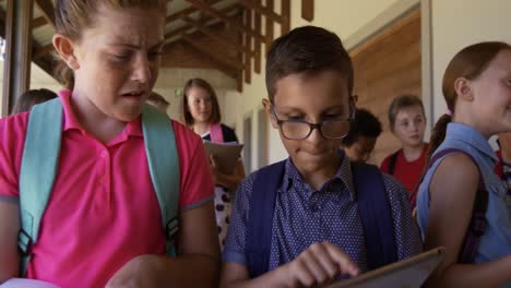 niño y niña discutiendo sobre una tableta digital en el pasillo de la escuela
