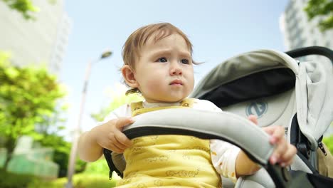 Das-Nachdenkliche-Gesicht-Eines-Kleinen-Kaukasischen-Blonden-Mädchens,-Das-An-Einem-Sonnigen-Tag-In-Einem-Kinderwagen-Sitzt