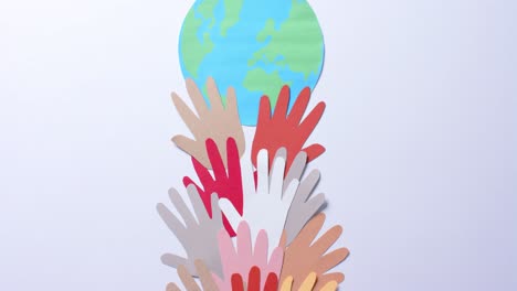 close up of hands together with globe made of colourful paper on white background with copy space