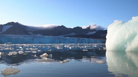 iceberg y pedazos de hielo en la laguna glacial bajo el glaciar y las colinas de las montañas de svalbard, noruega