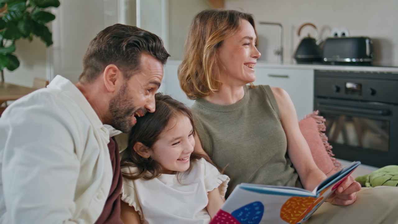 Primo piano di una famiglia sorridente che legge un libro seduta su un comodo divano a casa. La bambina si sta divertendo