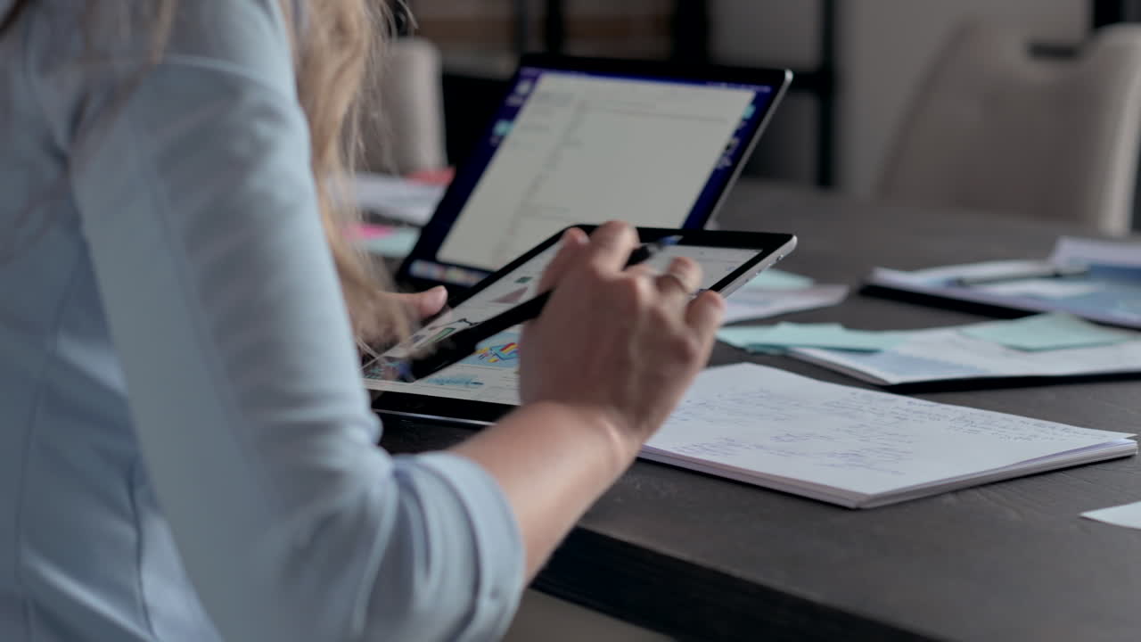 Woman in blue blazer working on a tablet and writing in a notebook at a desk in an office