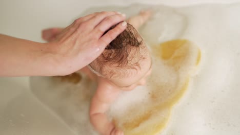 las manos de la madre frotan la cabeza del bebé con champú