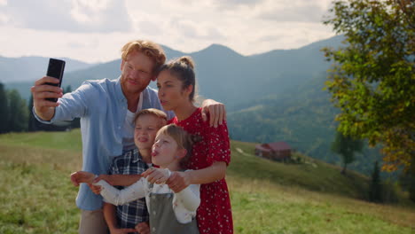 Joyful-family-taking-selfie-with-sticking-tongues-on-hill.-Parents-kids-have-fun