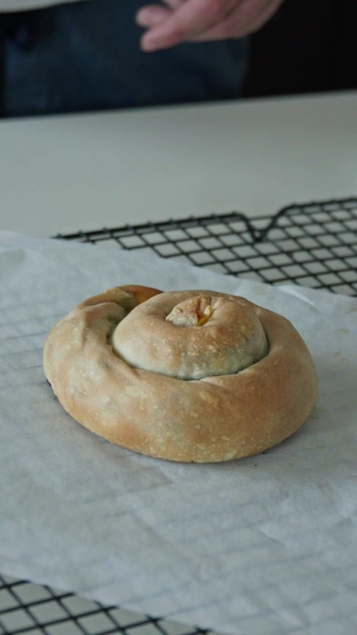 Homemade spiral spanakopita cooling on parchment paper after baking, with golden flaky pastry and rustic Greek pie presentation. Vertical close up shot.