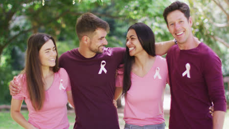 portrait of happy, diverse group of men and women wearing cancer awareness ribbons embracing in park