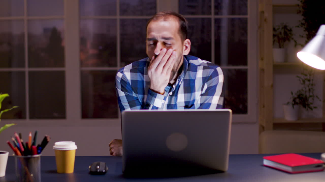 Tired man yawning in front of laptop at night