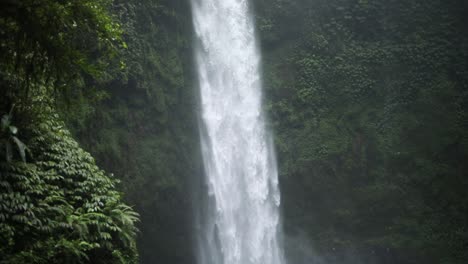 slow motion panning down shot in front of a gushing nungnung waterfall in bali, indonesia following a rain storm