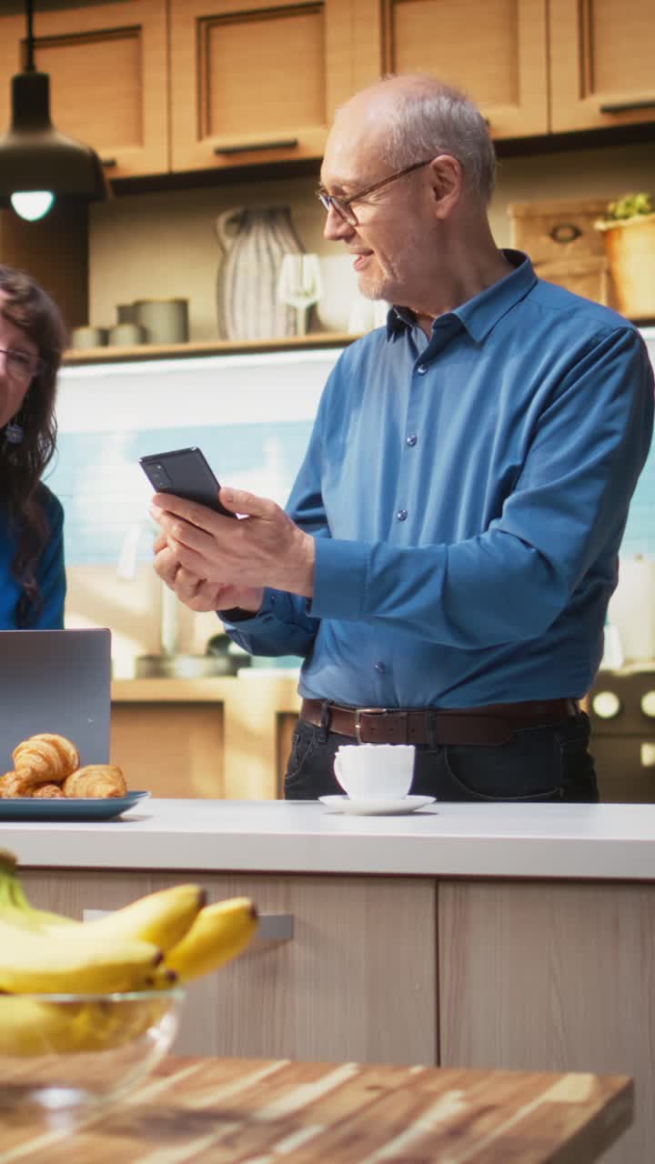Vertical Video Senior couple checking smartphone apps in home kitchen with a relaxed smile