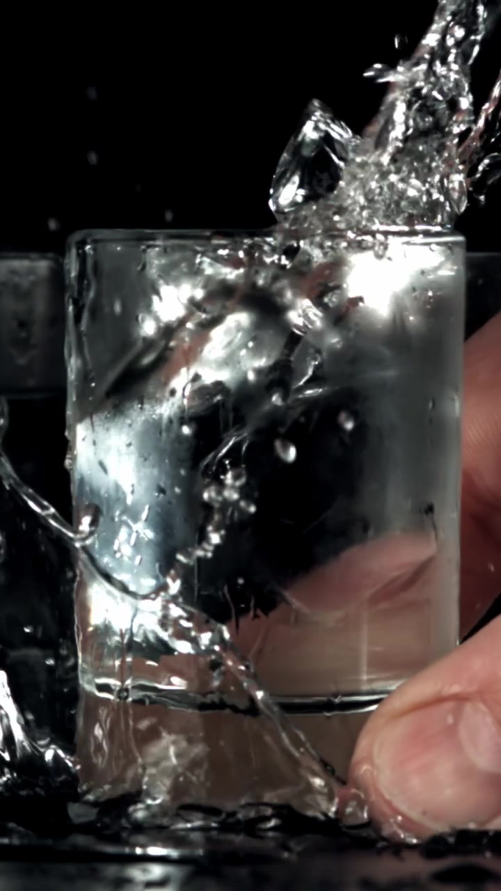 Primo piano di una mano che lascia cadere un bicchierino, provocando uno schizzo d'acqua al rallentatore