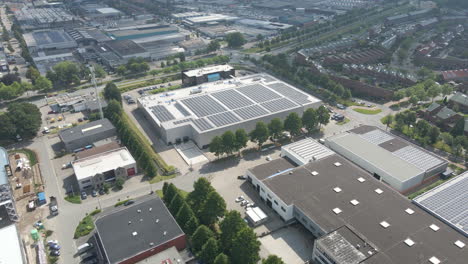 cinematic aerial - flying towards large industrial building with many photovoltaic solar panels on rooftop