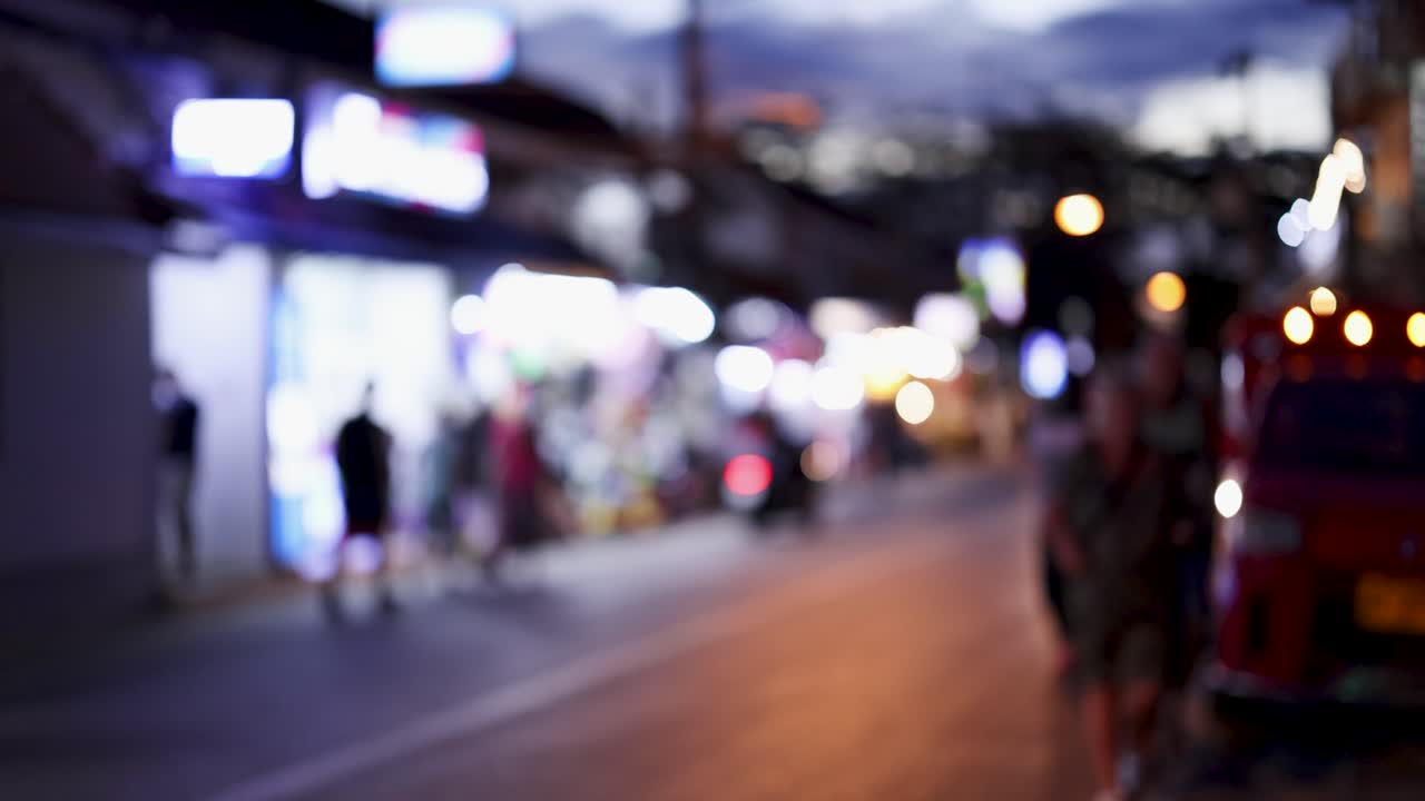 Blurred nighttime street scene in Phuket, Thailand, featuring tourists and vibrant lights, captured with a dynamic camera movement